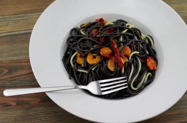 İtalyan siyah spagetti, alla Veneziana, ızgara karides ve kurutulmuş domates ile. Zeytinyağı, sarımsak ve etkisi için birkaç beyaz spagetti ile.