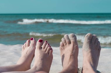 Deniz kenarında oturan dinlendirici çiftin bacakları. 