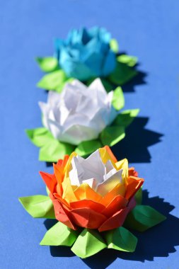 Mavi arka planda üç origami kağıdı, zambak çiçeği.