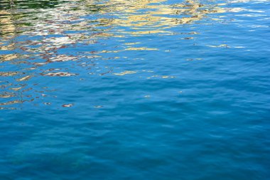 Suyun berrak mavi yüzeyi çarpık sarı ve beyaz renkleri yansıtır. 