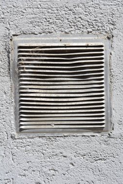 Tozlu, yıpranmış beyaz bir havalandırma gri, desenli bir duvara kurulur, aşınma ve yırtık izleri gösterir.