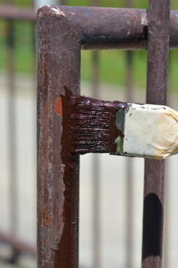 Boya fırçası, metal bir çit direğine yeni boyanmış kahverengi boya sürükler.