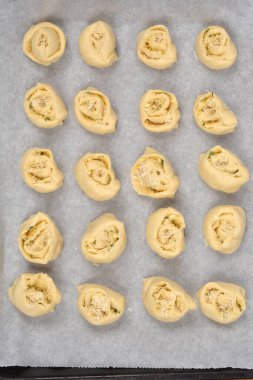 Yukarıdan bakıldığında sarımsak ve parmesanla dolu fırınlanmamış ruloların parşömen kağıdıyla kaplı bir çarşaf üzerinde sıralandığı görülüyor.