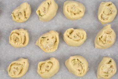 Yukarıdan bakıldığında sarımsak ve parmesanla dolu fırınlanmamış ruloların parşömen kağıdıyla kaplı bir çarşaf üzerinde sıralandığı görülüyor.