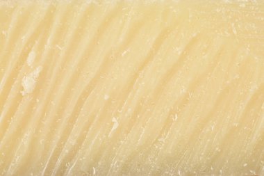 Bir kalıp parmesan peynirinin ayrıntılı yakın çekimi. Görünür çapraz çizgileri ve kaba bir dokusu var.