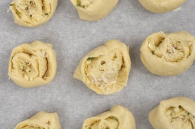 Yukarıdan bakıldığında sarımsak ve parmesanla dolu fırınlanmamış ruloların parşömen kağıdıyla kaplı bir çarşaf üzerinde sıralandığı görülüyor.