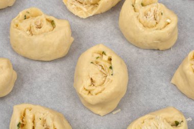 Yukarıdan bakıldığında sarımsak ve parmesanla dolu fırınlanmamış ruloların parşömen kağıdıyla kaplı bir çarşaf üzerinde sıralandığı görülüyor.