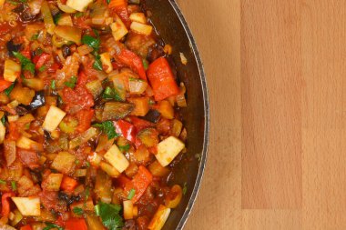 Tepetaklak bir İtalyan Caponata 'sının tepeden tırnağa görüntüsü, lezzetli bir patlıcan güveci ve tavada diğer sebzeler, ahşap bir arka plan ve kopyalama alanı.