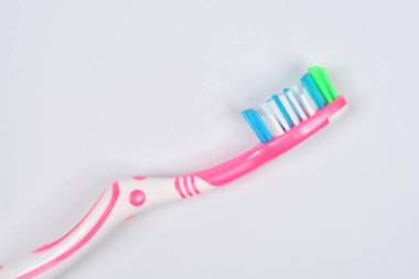 Pembe ve beyaz bir diş fırçasının çok renkli kılları olan, düz beyaz bir arkaplanda köşegenli bir yan görüntüsü.