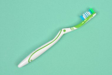 Yeşil ve beyaz bir diş fırçasının yukarıdan aşağı görüntüsü, çok renkli kıllarla, açık yeşil arka planda, kopyalama alanı ile çapraz olarak yatar.