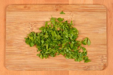 Tahta bir kesme tahtasının üzerinde taze doğranmış maydanoz yığını var.