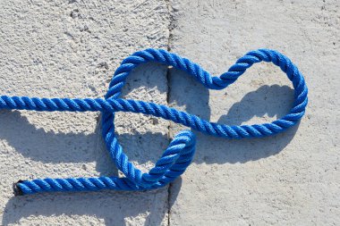 Gri, desenli beton bir yüzeyde uzanan parlak mavi bir ip basit ve grafik bir kompozisyon oluşturuyor.