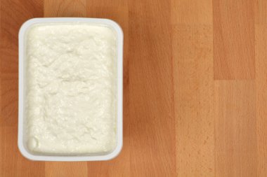 Açık kremalı taze peynir paketi ahşap bir arka plana konur ve yenmeye hazırdır.