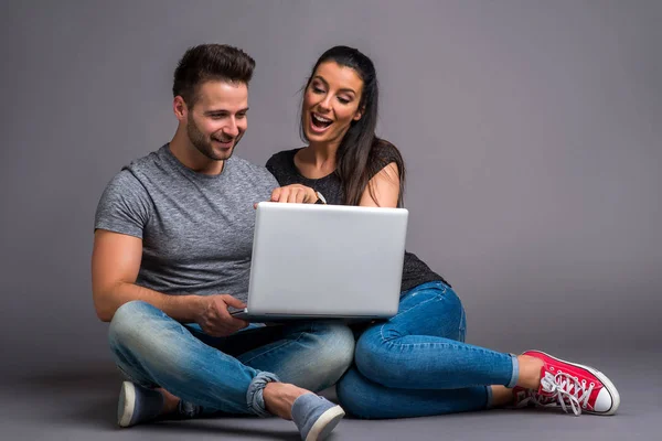 地面に座って ノート パソコンを見ていると笑みを浮かべて美しい若いカップル — ストック写真