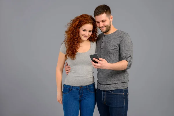 Jovem Bonito Abraçando Sua Bela Namorada Ambos Olhando Para Smartphone — Fotografia de Stock