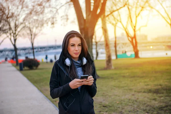 彼女の携帯電話を使用しながら夕日に公園を歩いて美しい若い女性 — ストック写真
