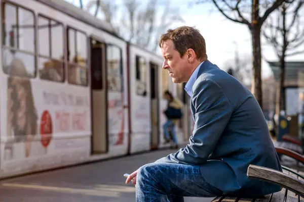 Medelålders Affärsman Sitter Bänk Spårvagnsstation Medan Håller Hans Smartphone Handen — Stockfoto