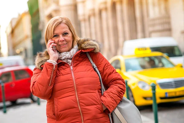 立っていると電話で話をしながら彼女をタクシーにしたい素敵な中年女性 — ストック写真