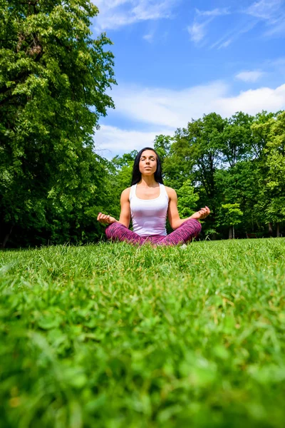 若くて美しいスポーティな女の子座っていると 公園の芝生の上で瞑想 レギンスとトップを着て — ストック写真