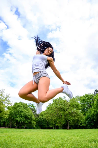ショートパンツとトップを着て公園のフィールドにジャンプする美しい若いスポーティーな女の子 — ストック写真