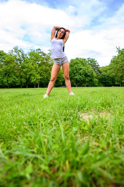 美しいスポーティーな少女 公園内のフィールドをストレッチ ショート パンツとトップを着て — ストック写真