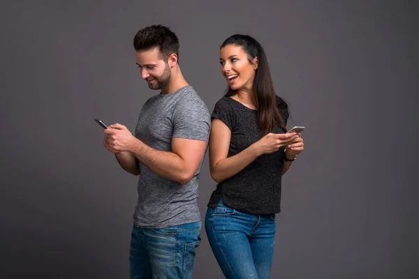 Beautiful Young Couple Standing Back Back While Holding Using Smartphone — Stock Photo, Image