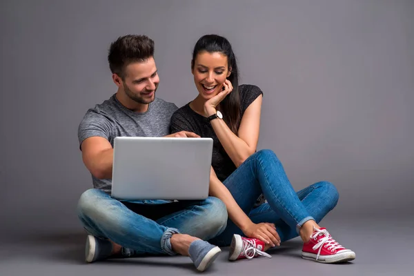 地面に座って ノート パソコンを見ていると笑みを浮かべて美しい若いカップル — ストック写真