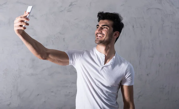 Un joven feliz tomando una selfie con su teléfono inteligente en un blanco — Foto de Stock