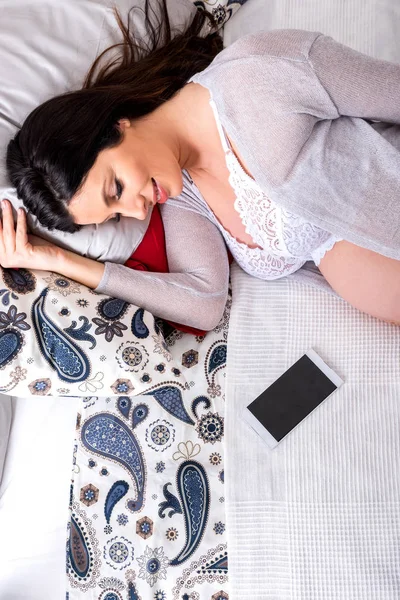 Een jonge zwangere vrouw liggend op een bed met een smartphone naast — Stockfoto