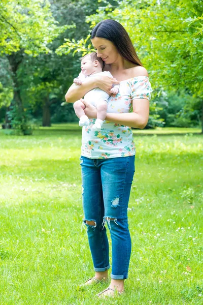 Una joven madre de pie en el parque y sosteniendo a su bebé — Foto de Stock