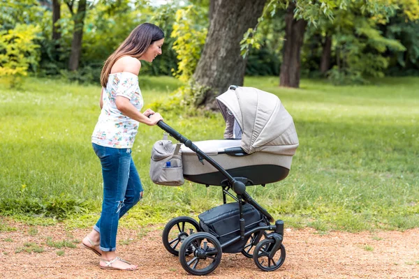 Μια νεαρή μητέρα περπατώντας με το μωρό της σε ένα καροτσάκι στο πάρκο — Φωτογραφία Αρχείου