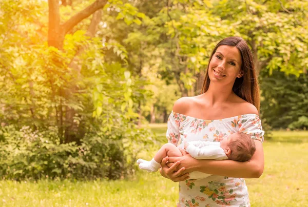 Молода мати стоїть в парку і тримає дитину — стокове фото