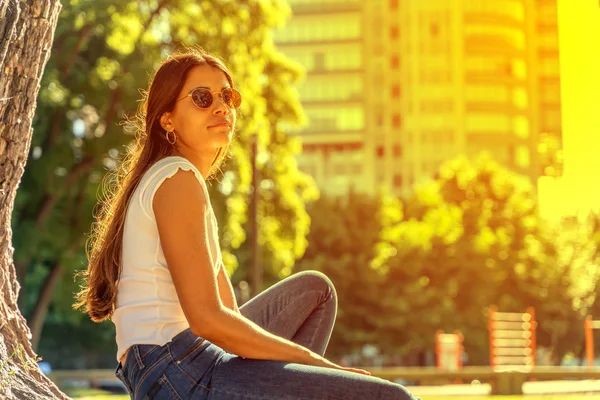 Młoda kobieta siedząca obok drzewa i ciesząca się słońcem — Zdjęcie stockowe