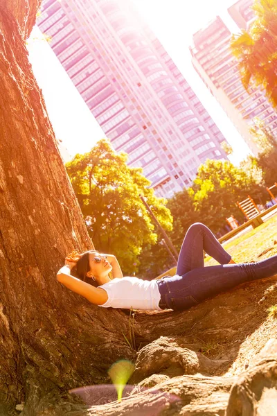 Una joven tumbada junto a un árbol y disfrutando del sol —  Fotos de Stock