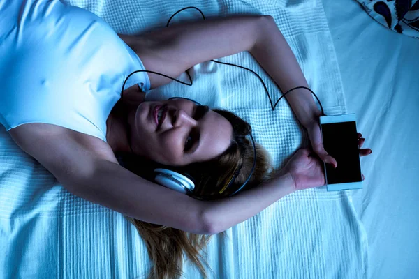 Usměvavá mladá žena leží na posteli a poslechu hudby — Stock fotografie