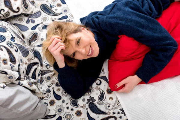 En leende ung kvinna liggande på en säng i en tröja — Stockfoto