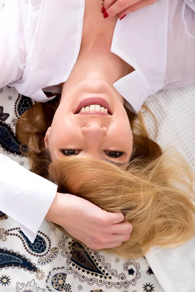 Счастливая молодая женщина лежит на кровати в белой рубашке — стоковое фото