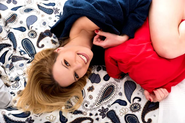 Een lachende jonge vrouw liggend op een bed in een trui — Stockfoto