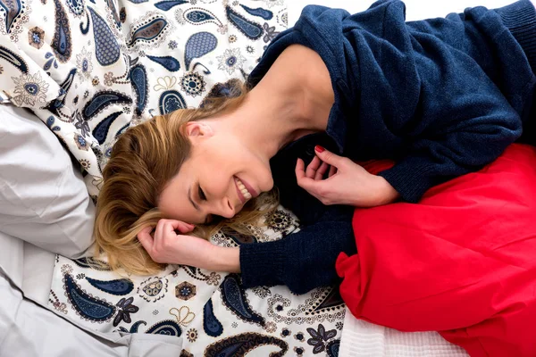A smiling young woman lying on a bed in a sweater — Stock Photo, Image