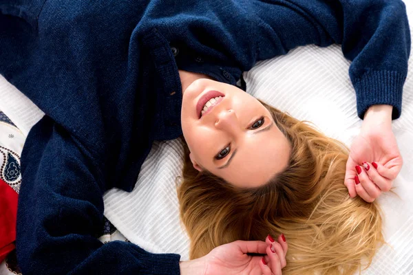 Улыбающаяся молодая женщина лежит на кровати в свитере — стоковое фото