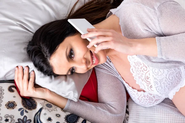 一名年轻的孕妇躺在床上, 用手机说话 — 图库照片