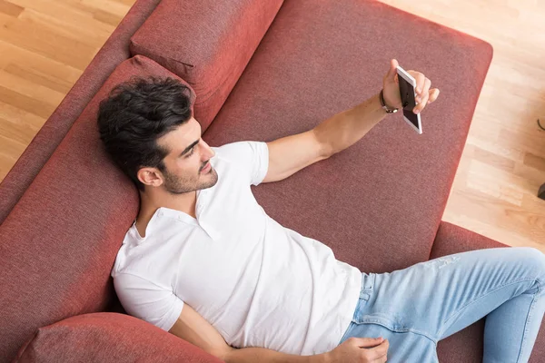 Un joven feliz tumbado en un sofá y tomando una selfie —  Fotos de Stock