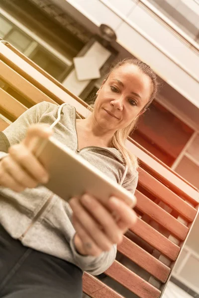 An athletic woman sitting on a bench and using her smartphone — Stock Photo, Image