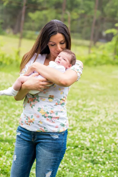 Una joven madre de pie y besando a su bebé — Foto de Stock