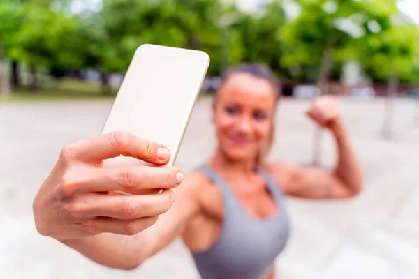 En atletisk kvinna tar en selfie och flexar i parken — Stockfoto