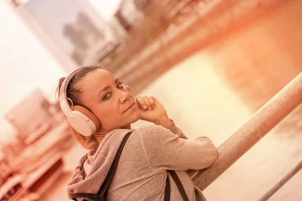 Uma mulher atlética ouvindo música ao lado do corrimão da ponte — Fotografia de Stock