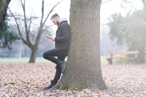 Hipster hombre apoyado en un árbol y la lectura — Foto de Stock