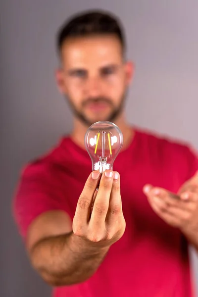 A young man in a red tshirt holding a lightbulb — Stock Photo, Image