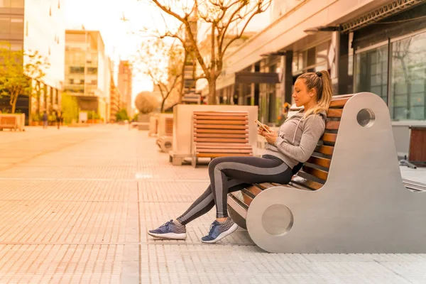 En atletisk kvinna sitter på en bänk och använda sin smartphone — Stockfoto