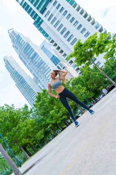 Una donna atletica con un top grigio che si lega i capelli nel parco — Foto Stock